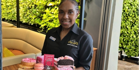 Image of young female First Nations Cowboys staff holding a plate of afternoon tea and smilingat the camera