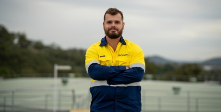 Image of Conor stevenson, smiling in yellow high vis shirt and navy pants, standing on top of a water tower