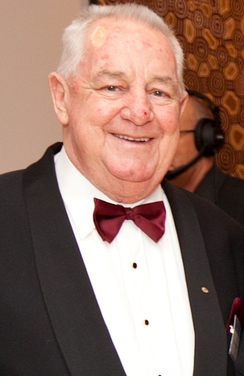 Image of Harry Hauenschild AO. Older male with white hair dressed in a black and white suit with a maroon bowtie 